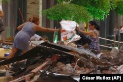 Personas rescatan pertenencias de entre los escombros de su vivienda derrumbadas tras un fuerte sismo en Machala, Ecuador, el sábado 18 de marzo de 2023. (AP Foto/Cesar Muñoz)