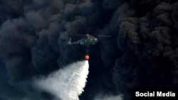 Un helicóptero derrama agua sobre uno de los tanques incendiados, mientras se eleva a la atmósfera una densa nube de humo. (Foto: Facebook MINSAP)