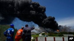 Trabajadores de Cuba Petróleo observan la larga columna de humo negro que se desprende del incendio en la base de supertanqueros de crudo, en Matanzas. (AP/Ramon Espinosa)