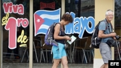Dos turistas pasan frente a un cartel alusivo al desfile que organiza el gobierno cubano el 1 de mayo.