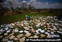 Una maestra seca libros al sol en La Coloma, Pinar del Río, de una escuela que resultó gravemente dañada por el huracán Ian. (AP Foto/Ramón Espinosa)