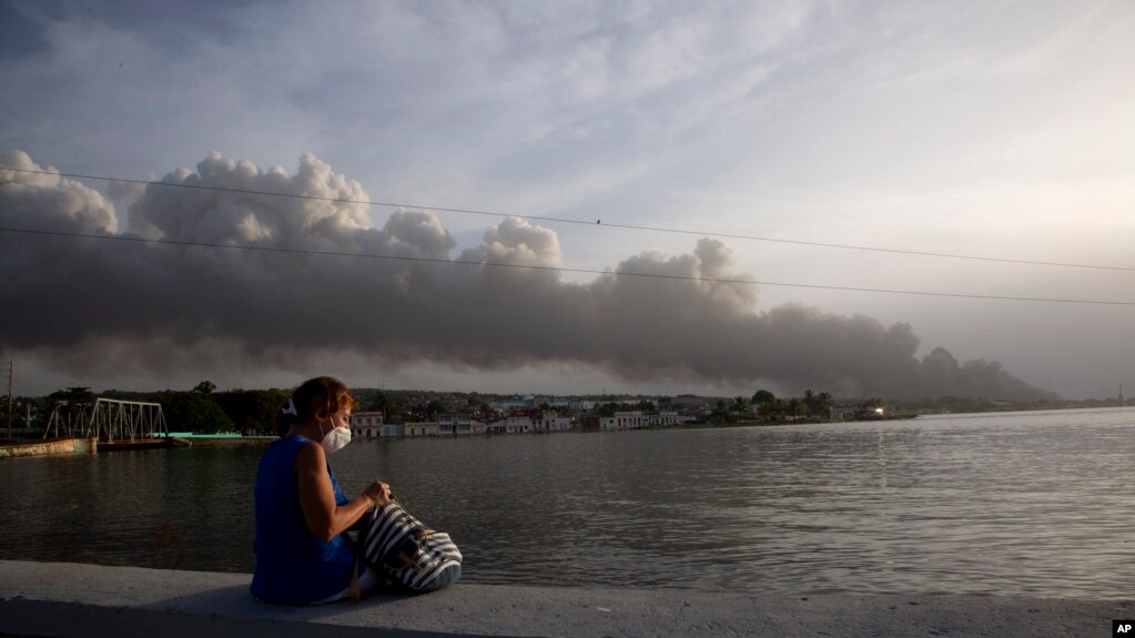 Una mujer contempla desde el malecón el humo del incendio en la Base de Supertanqueros de crudo en la Bahía de Matanzas, este martes, 9 de agosto. (AP Foto/Ismael Francisco)