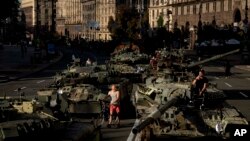 Varias personas caminan entre vehículos militares rusos destruidos instalados en el centro de Kiev, Ucrania, el 24 de agosto de 2022. (AP Foto/Evgeniy Maloletka)