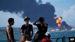 Jóvenes observan la columna de humo que se eleva del sitio de la catástrofe, en la zona industrial de Matanzas. Las autoridades advierten del peligro de contaminación. (AP/Ramon Espinosa).