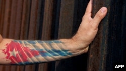 Un hombre con la bandera cubana tatuada en el brazo toca una de las barras de la cerca de la frontera de EEUU con México, en Ciudad Juarez. (Photo by HERIKA MARTINEZ/AFP/Archivo)