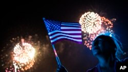 Una mujer observa los fuegos artificiales y sostiene una bandera de los Estados Unidos durante la celebración del 4 de julio. 