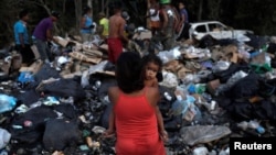 La venezolana Astrid Prado, carga a su hija de un año, en un basurero.