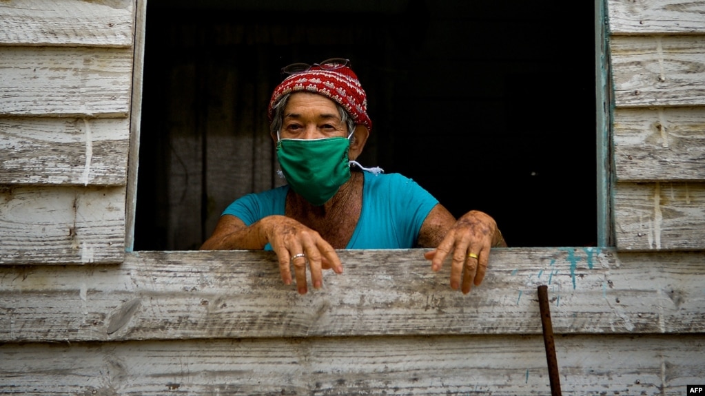 Una anciana de Zaragoza, en Mayabeque, se protege del coronavirus con un nasobuco mientras observa el camino desde su ventana. (Yamil Lage/AFP)