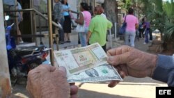 Un hombre muestra un peso convertible cubano y un dólar estadounidense frente a una oficina de Western Union en La Habana (Cuba).