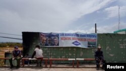 Trabajadores sentados frente a un cartel del gobierno en Matanzas, Cuba, el 10 de agosto de 2022. (Reuters/Alexandre Meneghini).