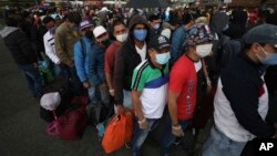 Viajeros en una terminal de Bogotá, Colombia, esperan en línea para abordar un ómnibus.
