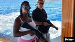 John McAfee junto a una mujer en su yate, sosteniendo armas de asalto. (Twitter/@officialmcafee)
