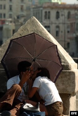 Una pareja de estudiantes se besan bajo una sombrilla en el malecón habanero.