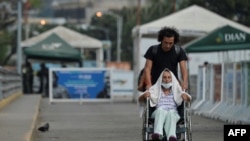Steve Oliveros conduce a su madre en silla de ruedas de vuelta a Colombia tras serle negado el paso en la frontera para entrar a Venezuela.