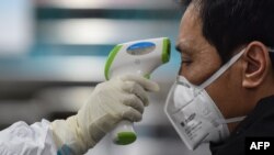 Un miembro de los servicios médicos chequea la temperatura de un paciente en un hospital de Wuhan, epicentro de la epidemia del coronavirus, el 25 de enero del 2020.