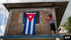 Una mujer cuelga una bandera cubana en su ventana.