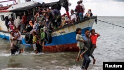 Ciudadanos locales ayudan a evacuar a refugiados Rohinyás de un bote que llegó a las costad de Indonesia