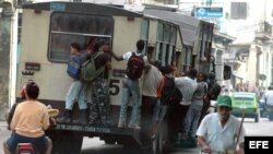 Varias personas viajan colgando de un ómnibus, popularmente conocido como camello