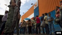 Un grupo de personas aguardan afuera del supermercado Día a Día para ingresar y hacer compras, bajo presencia militar, en la ciudad de Caracas (Venezuela).