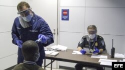 Oficiales de la Oficina de Aduanas y Protección Fronteriza de EEUU interrogan a un viajero y le toman la temperatura.