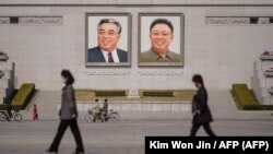 Ciudadanos norcoreanos caminando frente a retratos de Kim Il Sung y Kim Jong Il