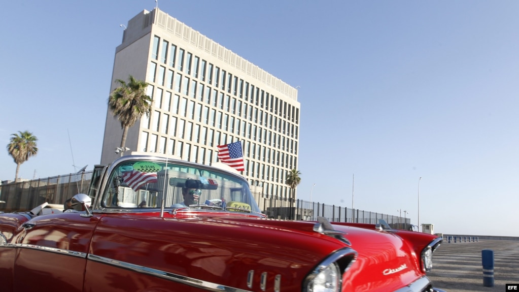 Un auto clásico pasa con una bandera de Estados Unidos frente a la embajada de ese país en La Habana.