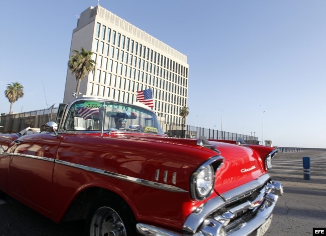 Un auto clásico pasa con una bandera de Estados Unidos frente a la embajada de ese país en La Habana.