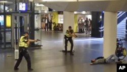 Dos policías holandeses apuntan sus armas hacia un hombre abatido a disparos por los agentes después de que éste apuñaló a dos personas en la estación central de trenes en Amsterdam.