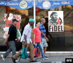 Varias personas camina por una calle en Santiago de Cuba, junto a imagen del líder de la revolución cubana Fidel Castro