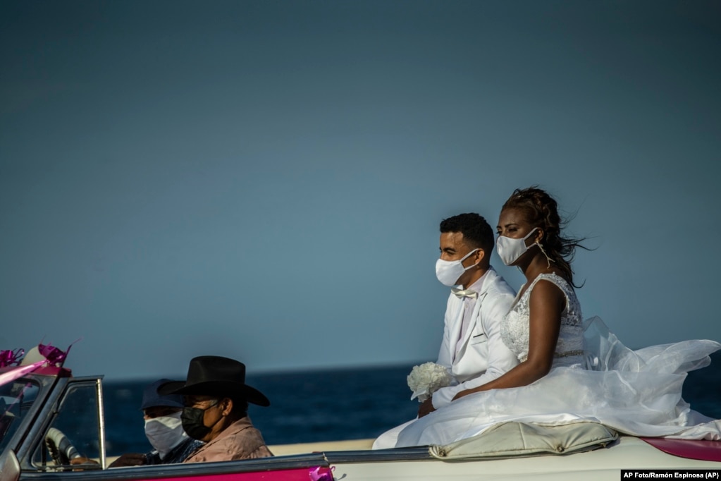 Ein frisch verheiratetes Paar fährt in einem amerikanischen Oldtimer den Malecon von Havanna entlang - mit Masken. | Bildquelle: Radio Televisión Martí | Bilder sind in der Regel urheberrechtlich geschützt