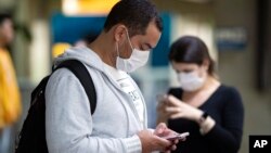 Pasajeros usando mascarillas como precaución contra el contagio del nuevo coronavirus usan sus teléfonos en el Aeropuerto Internacional de Sao Paulo, Brasil.
