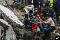 Equipos de rescatistas trasladan a una persona en camilla desde un edificio derruido por el sismo en Adana, Turquía. (IHA agency via AP)