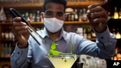 Con una máscara para protegerse del nuevo coronavirus, el cantinero Dagoberto Jesús Morejón prepara un "Martini de Oro", un cóctel con una planta endémica de Cuba llamada "Orozus de la Tierra".
