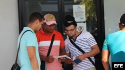 Tres cubanos revisan sus documentos, los cuales les permetirán comprar el boleto de avión para viajar a México.
