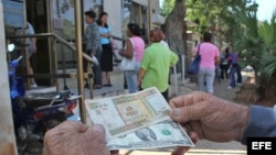 Un hombre muestra un peso convertible cubano y un dólar estadounidense frente a una oficina de la Western Union en La Habana.