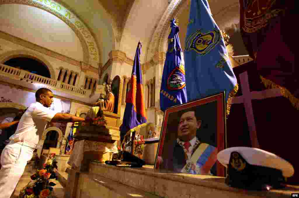 Vista de gorras militares colocadas a manera de ofrendas junto a un retrato del presidente de Venezuela, Hugo Chávez, en la iglesia Jesús de Miramar, en La Habana.