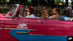 Turistas disfrutan de un mojito mientras viajan en un automóvil americano clásico durante un recorrido por la ciudad de Varadero (AP / Ramón Espinosa)