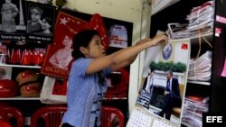 Una mujer de la Liga Nacional por la Democracia (NLD) cuelga un calendario con la fotografía de la opositora birmana Aung San Suu Kyi y el presidente de Estados Unidos en la tienda de recuerdos del partido en Rangún (Birmania).
