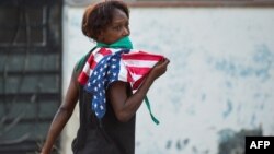 Una mujer con una máscara protectora contra el coronavirus y una bandera de EEUU camina por una calle de La Habana. (Yamil Lage/AFP)