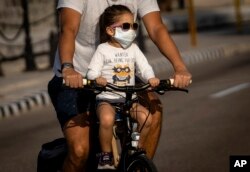 Una niña transportada en bicicleta usa un nasobuco para evitar el contagio del coronavirus, en La Habana.