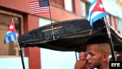 El conductor de un bicitaxi, adornado con banderas de Cuba y EEUU, espera la llegada de clientes en La Habana.