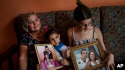 Danmara Triana (izquierda), con sus hijas Alice (centro) y Claudia, muestran fotos suyas con su hermano y su padre, quienes emigraron a Estados Unidos en 2015. (AP Foto/Ramón Espinosa)