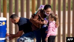 Una migrante cubana le da agua a su hija tras cruzar la frontera por el muro que separa a Estados Unidos y México, en Yuma, Arizona. (RINGO CHIU / AFP/Archivo)