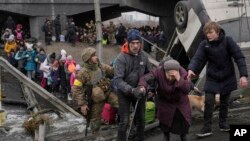 Una anciana es ayudada a cruzar el río Irpin sobre un camino improvisado bajo un puente que fue destruido por las tropas ucranianas para demorar un avance militar ruso, cerca de Irpin. (AP Foto/Vadim Ghirda)