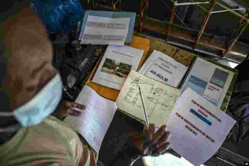 Adolfo Rivera muestra los planos y la documentación de su avión biplaza de madera, construido en el garaje de su edificio de departamentos en La Habana, Cuba, el viernes 19 de febrero de 2021. (AP Foto/Ramón Espinosa)